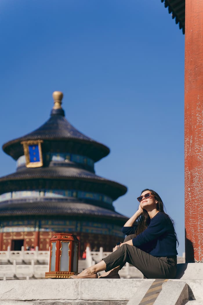 Turista sentada contemplando el Templo del Cielo en Beijing, China, bajo un cielo azul despejado.